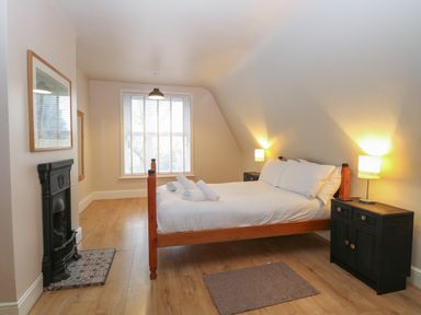 A bedroom with a wooden bed white bedding two black nightstands lamps a fireplace and a window at Grosvenor House in Kirkley Rise