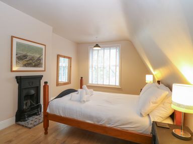 A bedroom with a wooden bed white bedding a window a mirror a fireplace and a lamp at Grosvenor House in Kirkley Rise