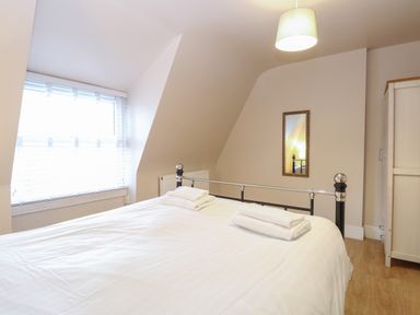 A bedroom with a double bed with towels on top a window with blinds a wall mirror a pendant light and a wardrobe at Grosvenor House in Kirkley Rise