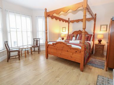 A bedroom with a wooden four-poster bed two wooden chairs and a small round table near large windows at Grosvenor House in Kirkley Rise