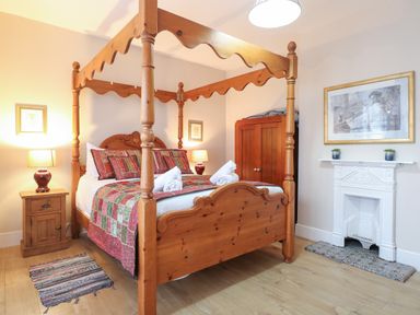 A bedroom with a wooden four-poster bed a wooden nightstand with a lamp a small rug a wooden wardrobe a white decorative fireplace and a framed artwork at Grosvenor House in Kirkley Rise