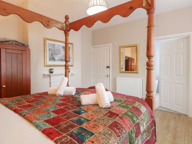A bedroom with a four-poster bed covered with a colorful patchwork quilt and rolled white towels on top a wooden wardrobe a framed picture above a white fireplace a mirror on the wall and doors leading to other rooms at Grosvenor House in Kirkley Rise