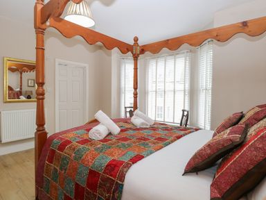 A bedroom with a four poster bed with rolled white towels on a colorful quilt at Grosvenor House in Kirkley Rise