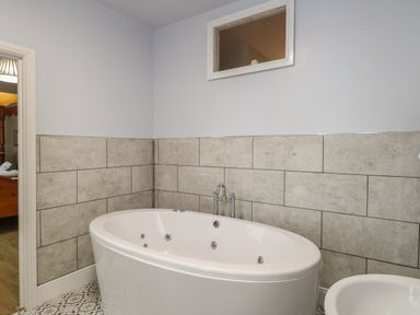 A bathroom with a white freestanding bathtub wall tiles and patterned floor at Grosvenor House in Kirkley Rise