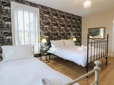 A bedroom with two beds a window with blinds a bedside table with lamps and a wall mirror at Grosvenor House in Kirkley Rise