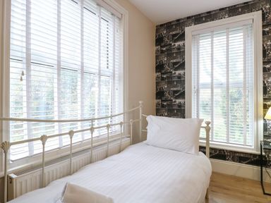 A bedroom with a white metal bed frame pillow and towel near two windows with white blinds at Grosvenor House in Kirkley Rise