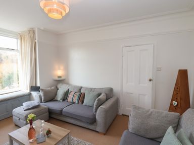 A living room with gray sofas a wooden coffee table and a window with curtains at Trackside Ruswarp
