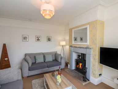 A living room with grey sofas a wooden coffee table a fireplace with a mirror above and a television mounted on the wall at Trackside in Ruswarp