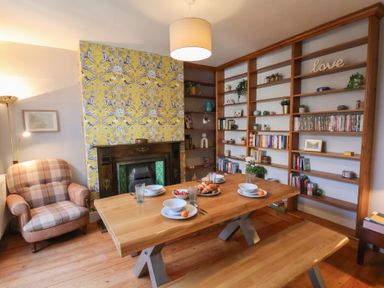 A dining room with a wooden table set for four and a bookshelf filled with books and decorations at Trackside in Ruswarp