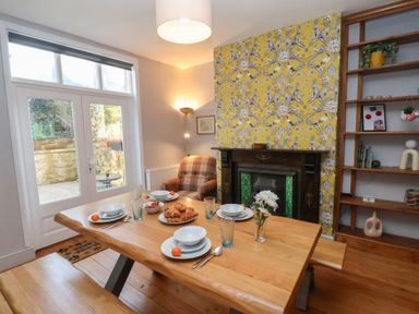 Dining area with wooden table set for four beside a fireplace and yellow patterned wall at Trackside in Ruswarp