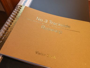 A brown spiral-bound visitor book with gold lettering on a desk at No 3 Trackside in Ruswarp