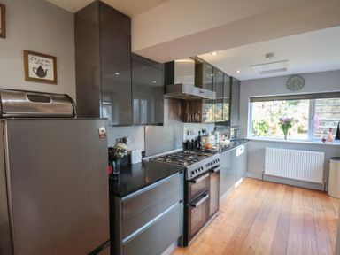 A kitchen with gray cabinets a stainless steel stove and oven a refrigerator and a window with flowers on the sill at Trackside in Ruswarp