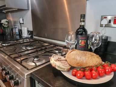 A kitchen countertop with a gas stove a plate with bread cheese tomatoes a bottle of Chianti wine and two wine glasses at Trackside in Ruswarp