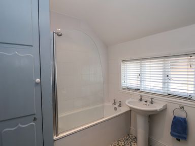 A bathroom with a bathtub shower combination a pedestal sink and a blue cupboard at Trackside in Ruswarp