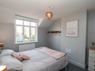 A bedroom with a double bed pillows and blanket near a window and dresser with flowers at Trackside in Ruswarp