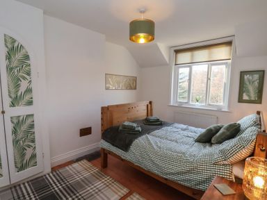 A bedroom with a wooden bed a window and a closet with leaf patterned panels at Trackside Ruswarp