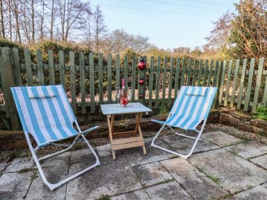 A patio with two blue and white striped chairs and a small wooden table with wine glasses and a bottle at Trackside in Ruswarp