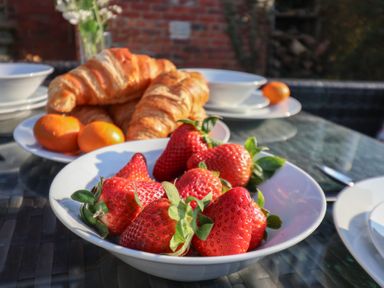 A bowl of strawberries and a plate with croissants and oranges on a glass table at Trackside Ruswarp