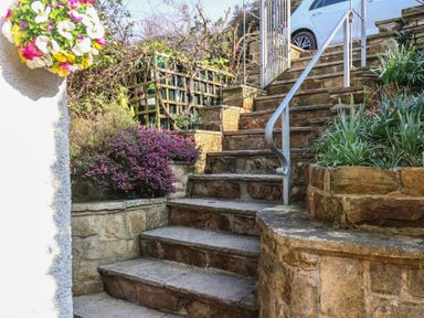 Stone steps with metal railing surrounded by plants and flowers leading to a white car at Trackside in Ruswarp