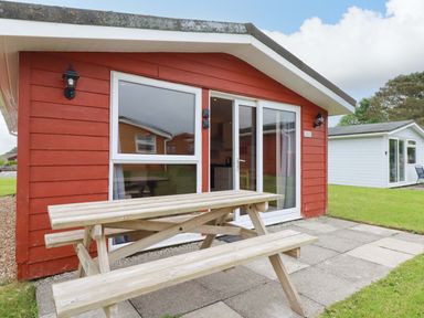 A red house with a wooden table and benches outside at 161 Atlantic Bay Holiday Park in Padstow