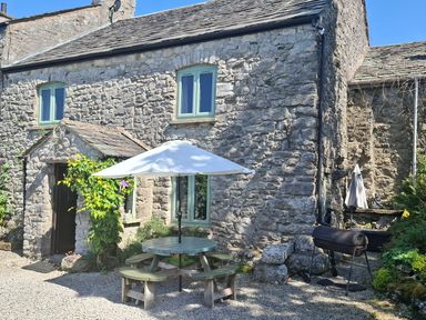 An outdoor area with a stone house, table, umbrella, and grill at The Old Farmhouse at Brackenthwaite Farm Yealand Redmayne near Arnside