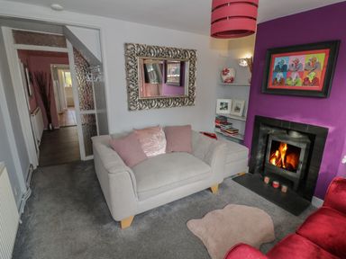A living room with a fireplace a beige sofa pink cushions and a purple wall at Cherry Blossom Cottage in Stratford-Upon-Avon