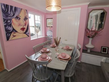A dining room with a wooden table set for four with pink dishes and a large portrait on the pink wall at Cherry Blossom Cottage in Stratford-Upon-Avon