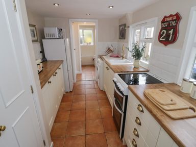 A narrow kitchen with wooden countertops white cabinets a stove a refrigerator a microwave and a washing machine at Cherry Blossom Cottage in Stratford-Upon-Avon