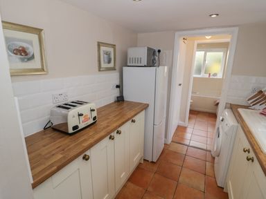 A narrow kitchen with wooden countertops toaster refrigerator and washing machine at Cherry Blossom Cottage in Stratford-Upon-Avon
