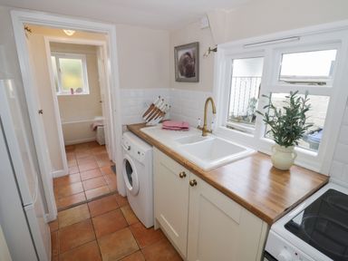 A kitchen with a washing machine a sink a potted plant and a view into a bathroom at Cherry Blossom Cottage in Stratford-Upon-Avon
