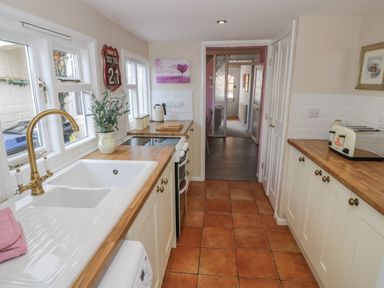 A narrow kitchen with wooden countertops a white sink and brass faucet a toaster and kettle on counters at Cherry Blossom Cottage in Stratford-Upon-Avon