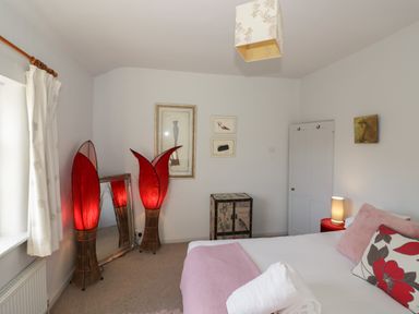 A bedroom with a bed and pillows a rolled towel two red lamps a mirror and framed pictures at Cherry Blossom Cottage in Stratford-Upon-Avon