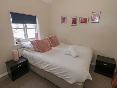 A bedroom with a bed and pink cushions and two black bedside tables at Cherry Blossom Cottage in Stratford-Upon-Avon