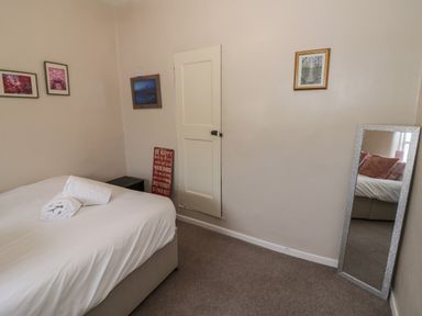 A bedroom with a bed a door wall pictures a mirror and towels at Cherry Blossom Cottage in Stratford-Upon-Avon
