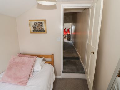 A bedroom with a single bed and pink pillows a framed picture on wall and an open door leading to a hallway at Cherry Blossom Cottage in Stratford-Upon-Avon