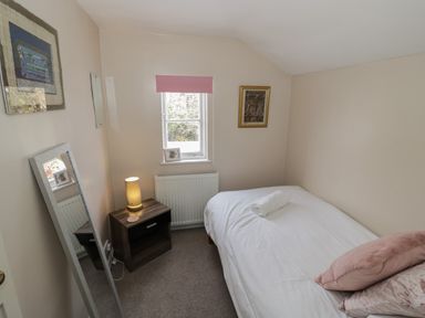 A bedroom with a single bed white linens pink pillows a bedside table with a lamp a window with a pink blind and wall art at Cherry Blossom Cottage in Stratford-Upon-Avon