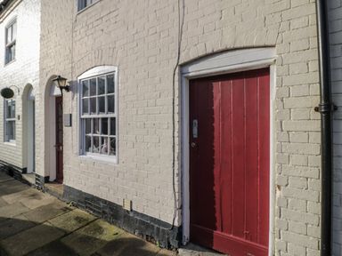 A white brick building with red doors and white framed windows on a stone pavement at Cherry Blossom Cottage in Stratford-Upon-Avon