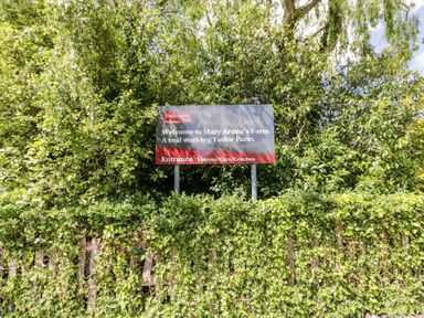 A sign welcoming visitors to Mary Arden's Farm a real working Tudor Farm surrounded by green foliage at Cherry Blossom Cottage in Stratford-Upon-Avon