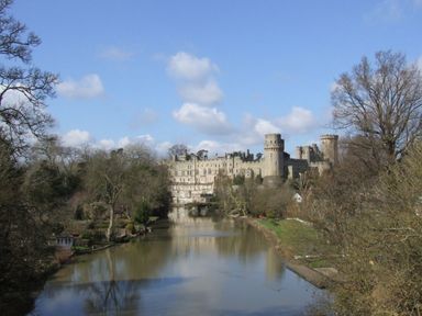 A river with trees on both sides and a castle in the background at Cherry Blossom Cottage in Stratford-Upon-Avon