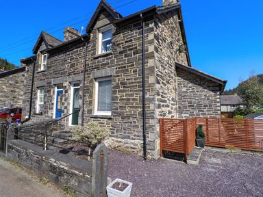 The exterior of a stone house with a blue door a small garden area and a wooden fence at Dola in Pentre Du near Betws-Y-Coed