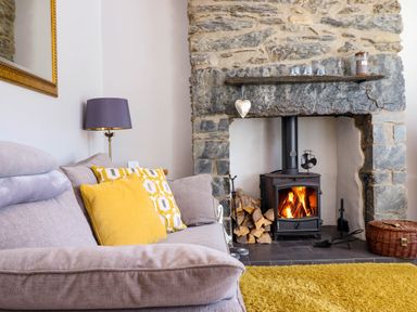 A living room with a sofa and cushions beside a stone fireplace with a wood burning stove and a yellow rug at Dola in Pentre Du near Betws-Y-Coed