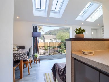 A dining area with table and chairs next to a balcony door with mountain view at Dola Pentre Du near Betws-Y-Coed