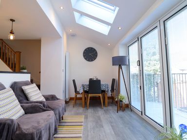 A dining area with a table and chairs next to large glass doors and a sofa with cushions in a living space at Dola in Pentre Du near Betws-Y-Coed