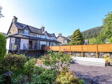 Stone and white house with garden and wooden fence surrounded by trees and hills at Dola in Pentre Du near Betws-Y-Coed