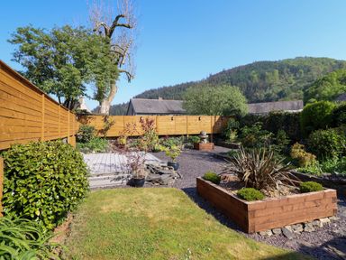 A garden with plants bushes and a wooden fence with hills in the background at Dola in Pentre Du near Betws Y Coed