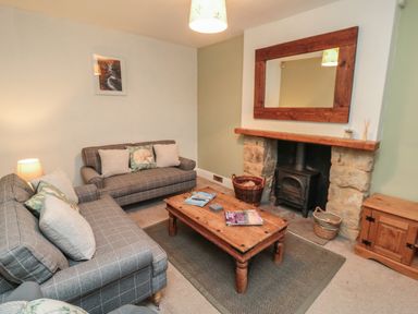 A living room with two sofas a wooden coffee table a stone fireplace with a wood stove a large wooden mirror and a wooden cabinet at Providence Cottage in Ugglebarnby near Sleights