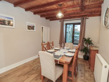 A dining room with a wooden table set with plates and glasses and wooden chairs at Providence Cottage in Ugglebarnby near Sleights