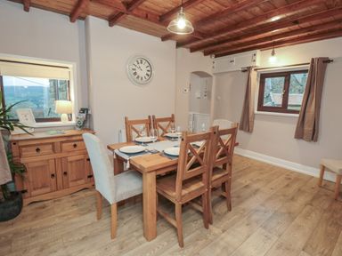 A dining room with a wooden table set for four and a wooden sideboard under a window at Providence Cottage Ugglebarnby near Sleights