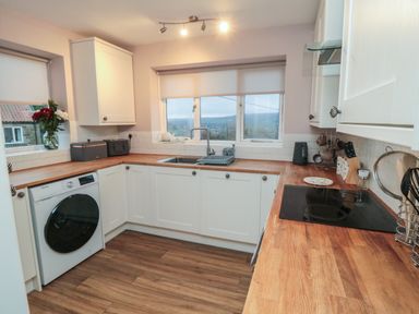 A kitchen with wood countertops white cabinets a washing machine a sink and windows at Providence Cottage in Ugglebarnby near Sleights