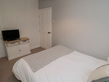 A bedroom with a bed a cabinet with a television and a closed door at Providence Cottage in Ugglebarnby near Sleights